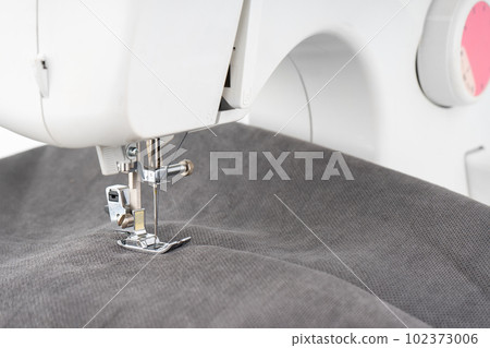 Modern sewing machine presser foot with gray fabric and thread, closeup 102373006