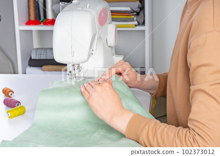 Female hands stitching white fabric on modern sewing machine at workplace in atelier 102373012