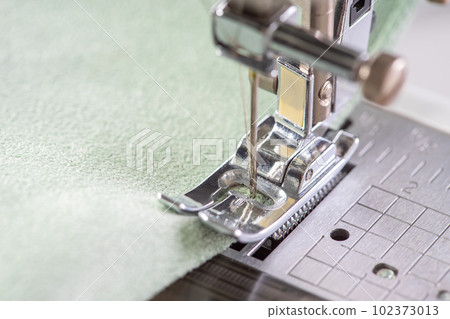 Modern sewing machine presser foot with green fabric and thread, closeup, macro Modern sewing machine presser foot with green fabric and thread, closeup, macro 102373013