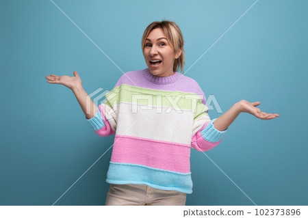 pleasant blond young woman in a striped sweater throws up her hands on a blue background pleasant blond young woman in a striped sweater throws up her hands on a blue background 102373896