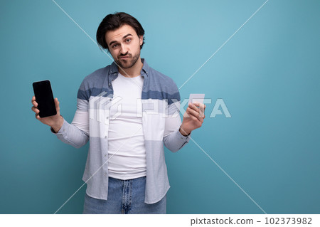upset young brunette man with credit card and smartphone upset young brunette man with credit card and smartphone 102373982