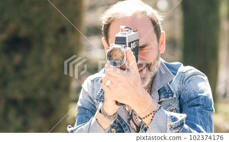 Mature man shooting video in city park with vintage camera Mature man shooting video in city park with vintage camera 102374176