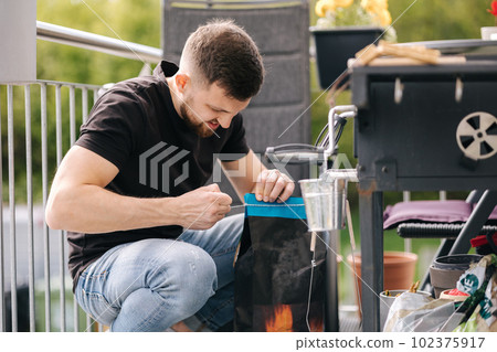 Man opens a package of charcoal for grilling. Preparing for barbecue on backyard  102375917