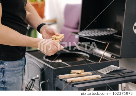 Close-up of man use fire briquettes for lighting a fire in the grill. Outdoor barbecue on terrace 102375973