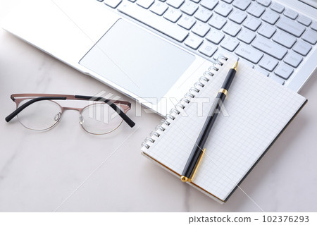 Image of desk work on a laptop while taking notes in a notebook Image of desk work on a laptop while taking notes in a notebook 102376293