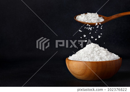 sea salt crystals falling from spoon in bowl on black background sea salt crystals falling from spoon in bowl on black background 102376822