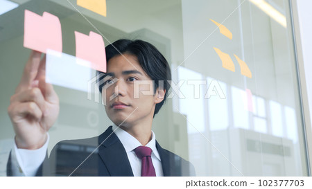 Businessman thinking while looking at sticky notes in the office Businessman thinking while looking at sticky notes in the office 102377703