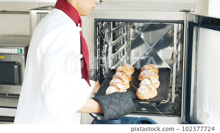 Baker taking bread out of the oven Baker taking bread out of the oven 102377724