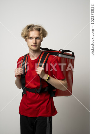 Courier delivers groceries home. Delivery man in red uniform with a thermal backpack isolated on a white background. Fast home delivery. Online order. 102378038