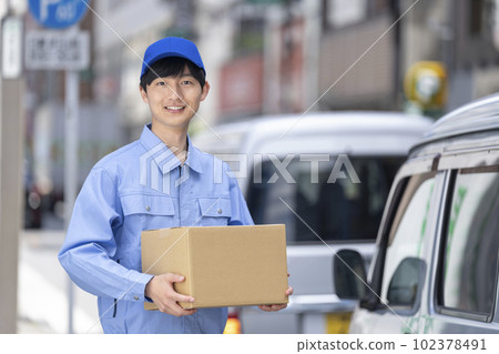 物流/送貨/運輸行業形像一個穿著工作服的男人在馬車旁邊拿著一個紙箱 102378491