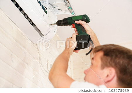 A man unscrews an air conditioner on the wall with a screwdriver 102378989