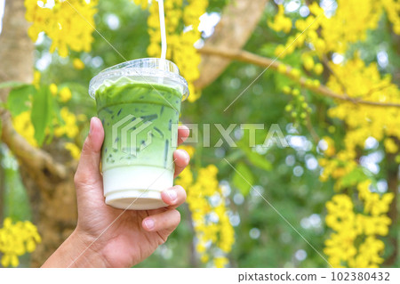 Woman hand holding the glass iced matcha latte green tea coffee on spring nature background 102380432