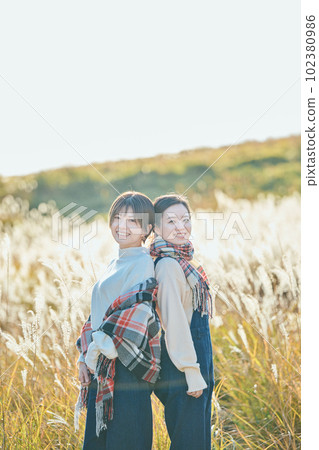 Young woman and her friend standing back to back against the background of pampas grass 102380986