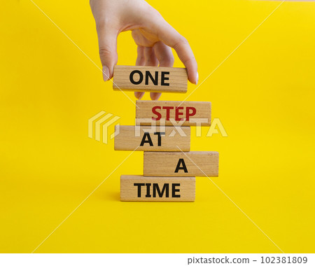 One step at a time symbol. Concept words One step at a time on wooden blocks. Beautiful yellow background. Businessman hand. Business and One step at a time concept. Copy space. One step at a time symbol. Concept words One step at a time on wooden blocks. Beautiful yellow background. Businessman hand. Business and One step at a time concept. Copy space. 102381809