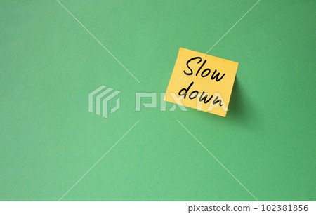 Slow down symbol. Orange steaky note with words Slow down. Beautiful green background. Business and Slow down concept. Copy space. 102381856