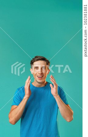 Surprised man. Expressive emotion. Astonished optimistic handsome guy in blue raised arms looking big amazed eyes isolated on turquoise copy space background. Surprised man. Expressive emotion. Astonished optimistic handsome guy in blue raised arms looking big amazed eyes isolated on turquoise copy space background. 102381881