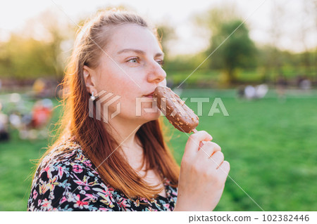 Happy young woman with delicious chocolate ice cream outdoors. Unhealhty food and weight loss concept. Summer time, eating 102382446