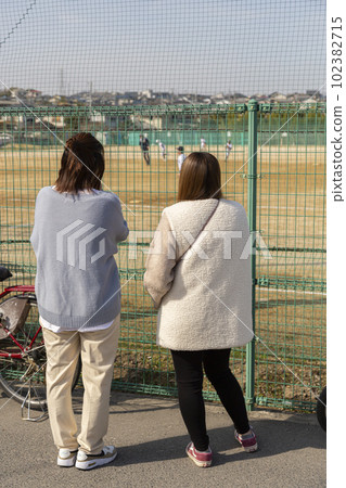 A woman (mother) watching youth baseball over the fence 102382715