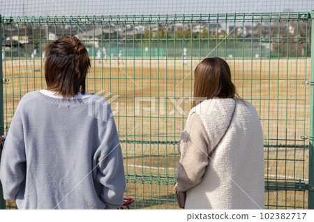 Mothers watching youth baseball through the fence 102382717