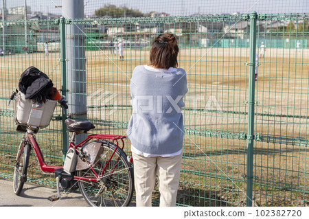 A mother watching youth baseball through the fence 102382720