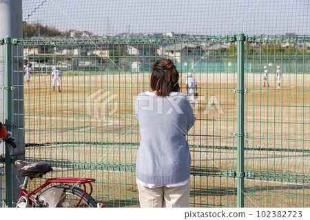 A mother watching youth baseball through the fence 102382723