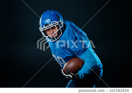 Portrait of a man in a blue uniform for american football on a black background. Portrait of a man in a blue uniform for american football on a black background. 102382834