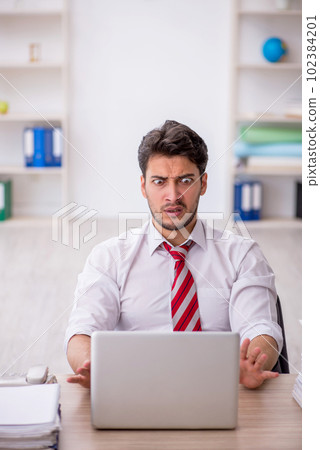 Young male employee and too much work in the office 102384201