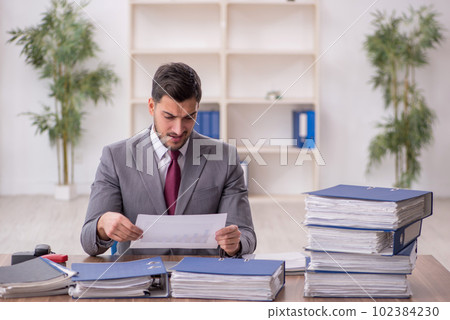 Young male employee and too much work in the office 102384230