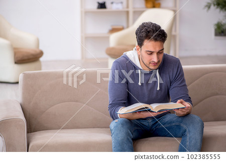 Young male student reading book at home Young male student reading book at home 102385555