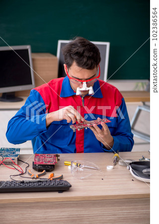 Young male repairman repairing computers in the classroom Young male repairman repairing computers in the classroom 102386564