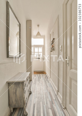 a hallway with wood flooring and white painted walls in the background is a mirror on the wall above it 102386753