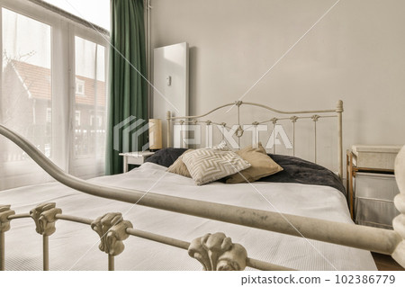 a bed in a bedroom with green curtains on the windowsills and an iron headboard that has been painted white 102386779