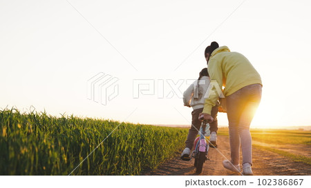 happy family. mother teaches little child to ride bicycle. in the park sunset. chidhood dream. ride a child bike in the sun. happy family life concept. child girl daughter rides road driving bicycle. 102386867