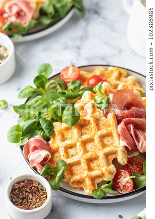 Cheesy belgian waffles served with ham, tomatoes and lettuce corn close up on white marble background . Savory waffles. Healthy breakfast 102386985