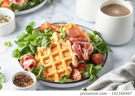 Cheesy belgian waffles served with ham, tomatoes and lettuce corn on white marble background . Savory waffles. Healthy breakfast 102386987