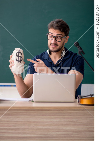 Young male music teacher holding moneybag in the classroom 102387857