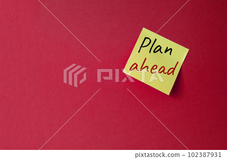 Plan ahead symbol. Orange steaky note with words Plan ahead. Beautiful red background. Business and Plan ahead concept. Copy space. Plan ahead symbol. Orange steaky note with words Plan ahead. Beautiful red background. Business and Plan ahead concept. Copy space. 102387931