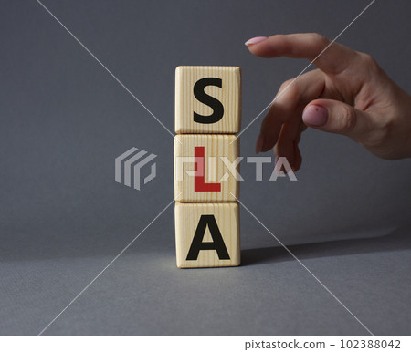 SLA - Service Level Agreement. Wooden cubes with word SLA. Businessman hand. Beautiful grey background. Business and Service Level Agreement concept. Copy space. 102388042