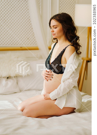 a slender pregnant woman in a black underwea and white shirt on the bed a slender pregnant woman in a black underwea and white shirt on the bed 102388965