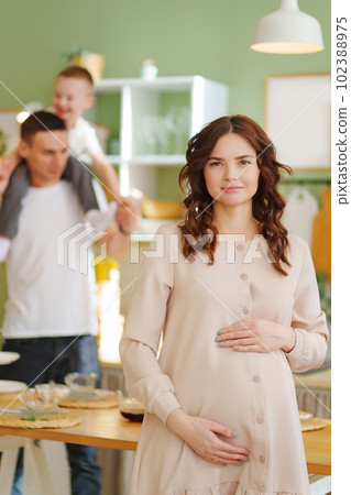 pregnant mom against the background of son and dad In the kitchen. pregnant mom against the background of son and dad In the kitchen. 102388975