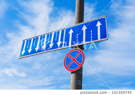 A traffic sign prohibiting car parking (red cross on blue circle) with an additional sign indicating lane distribution (multi-lane traffic) - white arrows in blue rectangle. 102389745