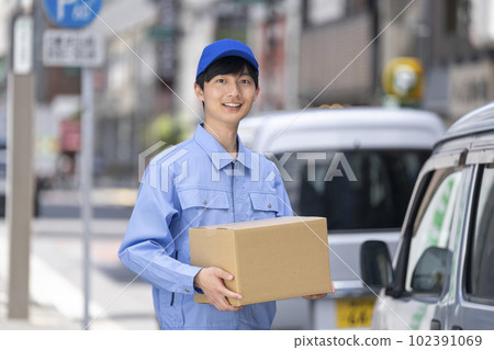 Logistics/delivery/transportation industry image A man in work clothes holding a cardboard box next to a wagon Logistics/delivery/transportation industry image A man in work clothes holding a cardboard box next to a wagon 102391069