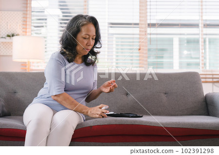 A senior woman's hand checking her blood sugar level with a glucometer by herself at her home. 102391298