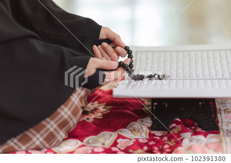 A close-up shot hands of a Muslim woman holding a rosary while wearing a long hijab, as she prays to the Muslim God, at the mosque during an Islamic religious ceremony. 102391380