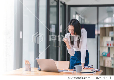 Happy and excited, a young asian woman student or office worker, celebrates achieving her goal of winning an online competition or receiving good news via email by raising hands in euphoria. 102391401