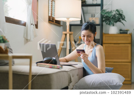 A happy young woman is shown shopping online using her laptop and credit card at home. 102391489