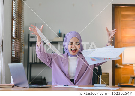 Portrait of a successful Muslim millennial businesswoman wearing a purple hijab and a stylish purple suit, throwing papers up in her office as she enjoys freedom from deadlines. Portrait of a successful Muslim millennial businesswoman wearing a purple hijab and a stylish purple suit, throwing papers up in her office as she enjoys freedom from deadlines. 102391547