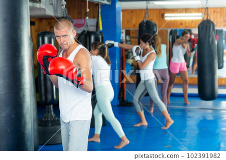 Young man in boxing gloves practicing punches on punchbag in gym 102391982