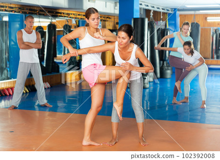 Young girl practicing elbow and knee strikes while locked arm with female opponent 102392008