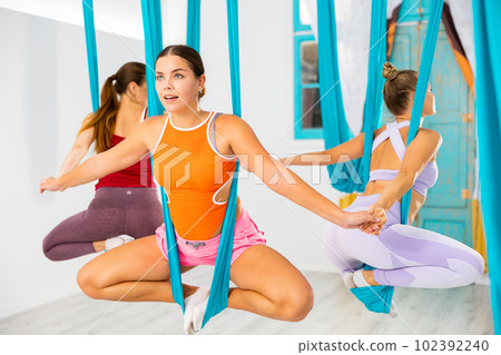 Girl doing butterfly pose in suspended hammock in circle with women Girl doing butterfly pose in suspended hammock in circle with women 102392240